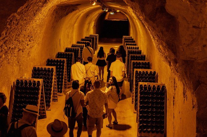 Champagne bottles stacked along a lit cellar passage