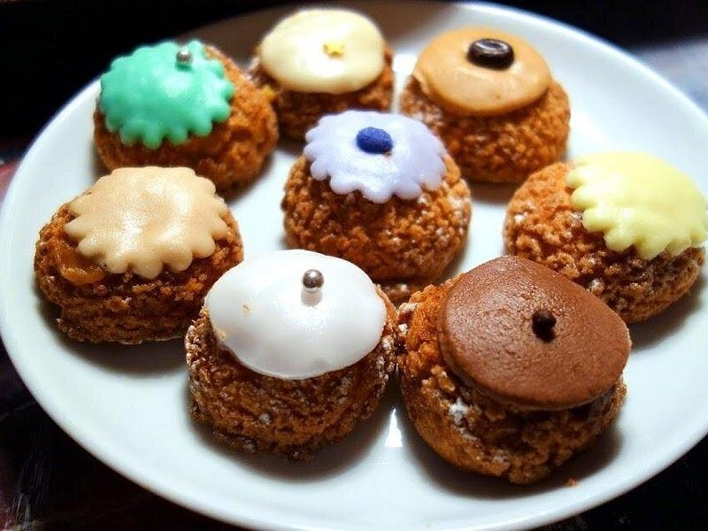 A plate of glazed choux pastries in pistachio, vanilla and chocolate
