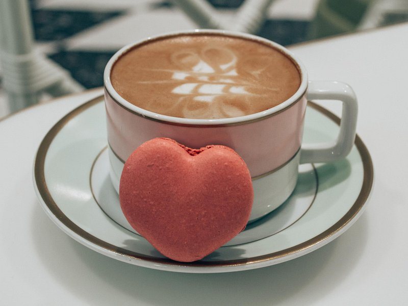 A cafe creme with a heart-shaped raspberry macaron in the saucer