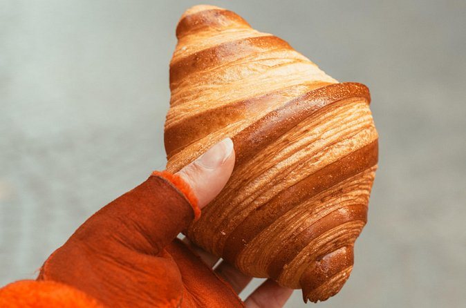 A croissant held up outside a Paris bakery, its layers showing at the tear