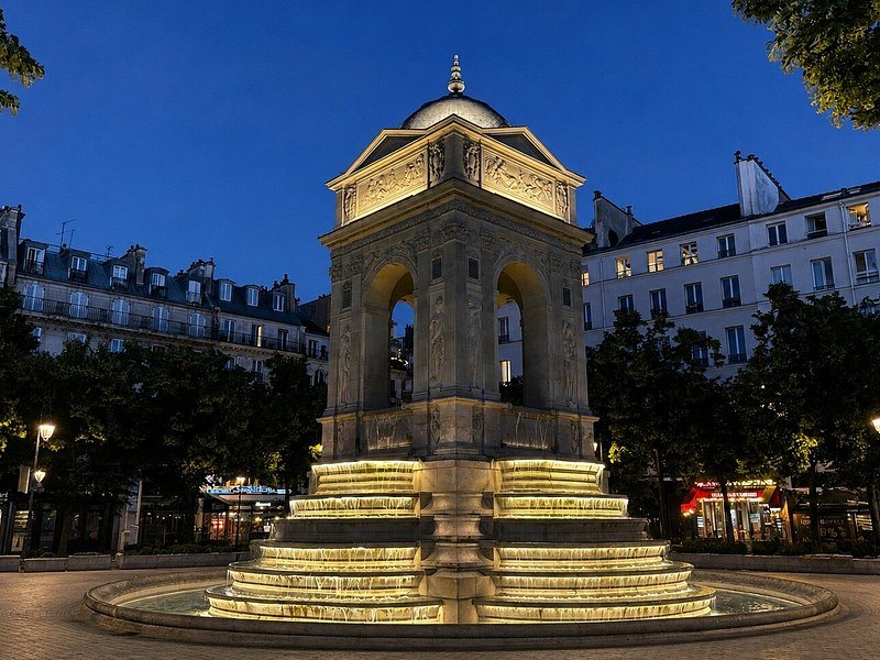 A lit Paris fountain at dusk with the square empty around it