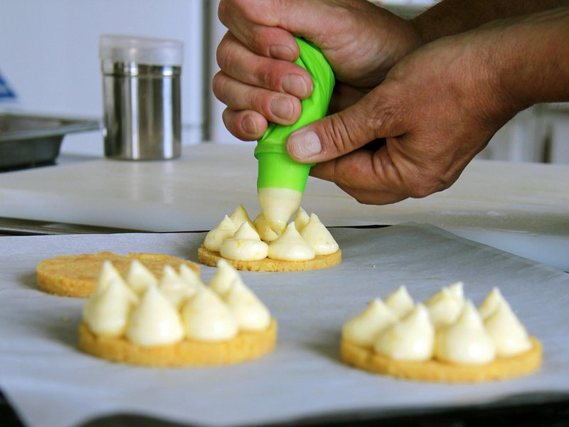 Cream being piped onto small pastry bases in a Paris kitchen